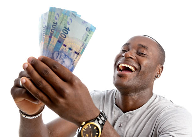 A man of African origin smiles in delight as he holds up a sheaf of South African One Hundred Rand  banknotes.